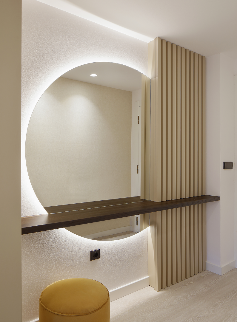 Espacio de recibidor en vivienda con un gran espejo circular retroiluminado, diseñado en un proyecto de interiorismo